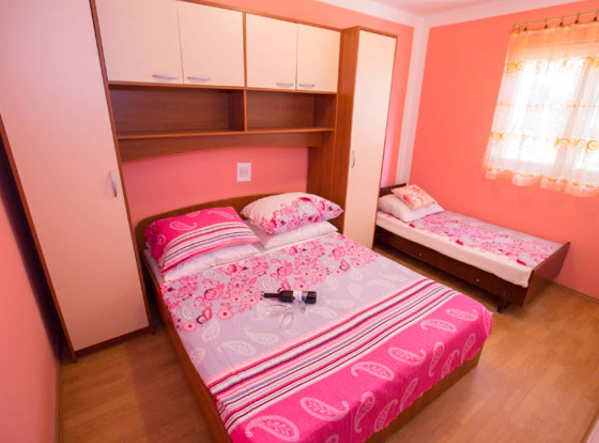 Ein Schlafzimmer mit zwei Betten, rosafarbenen Wänden und einem Kleiderschrank.