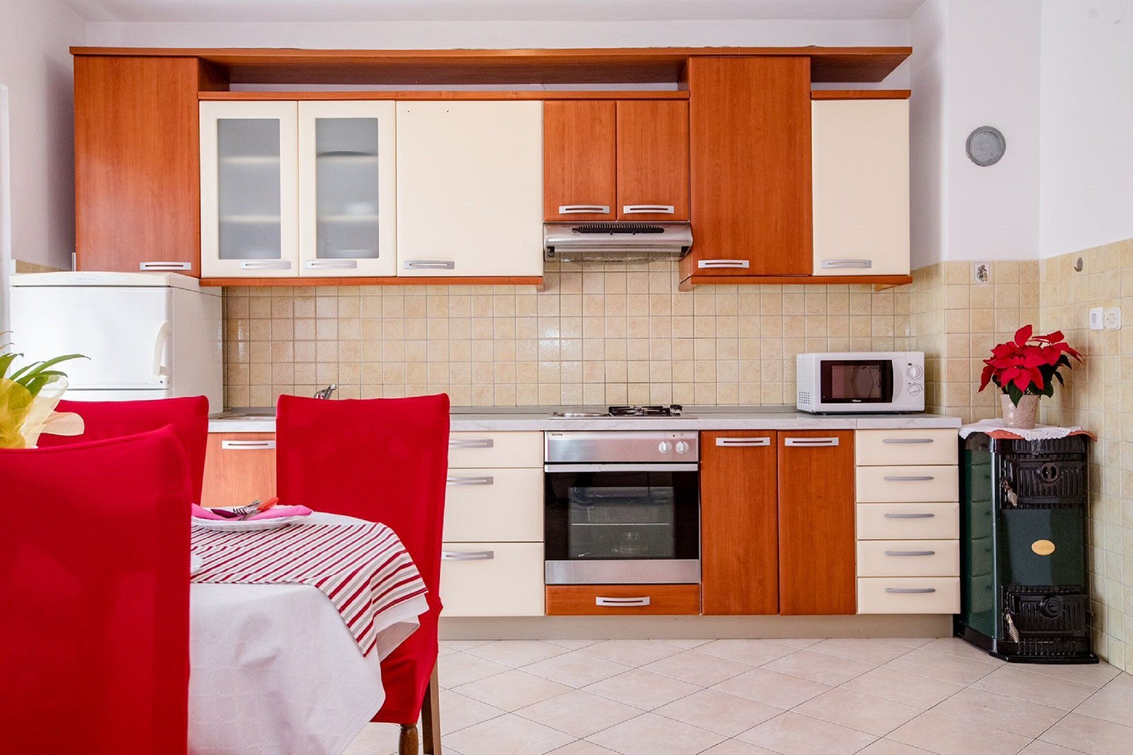 Een compacte keuken met houten kastjes, een magnetron, een oven en een eethoek met een tafel en stoelen.