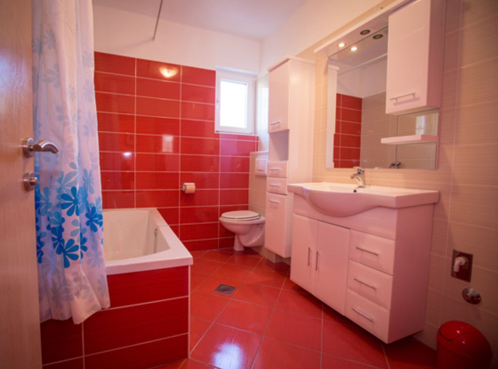 A bathroom with red tiles, a white bathtub, a white sink, and a white toilet.