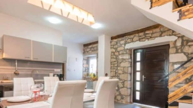 A modern living room with a dining area, stone wall, and staircase.