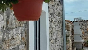A stone wall with a hanging red pot and a white vertical structure.