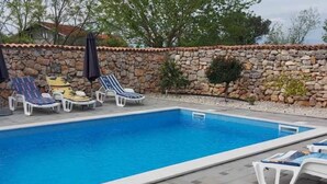 A rectangular swimming pool with a stone wall and tiled deck.