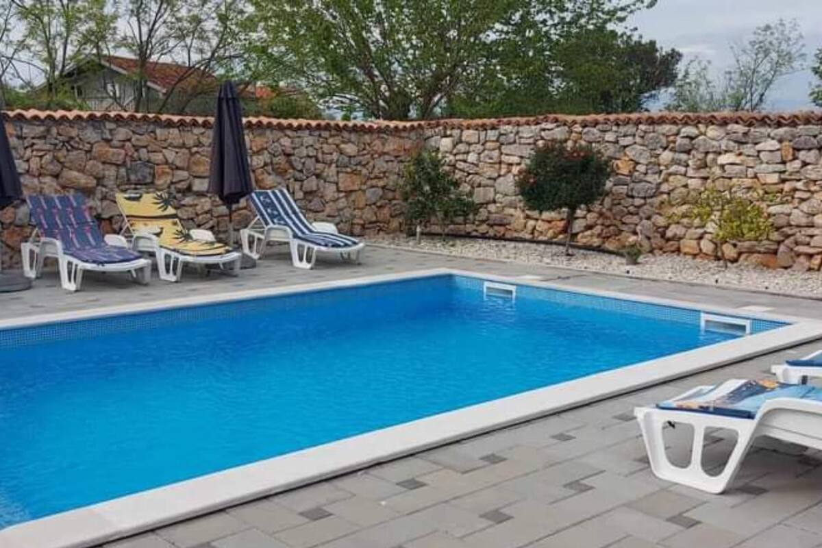 A rectangular swimming pool with a stone wall and tiled deck.