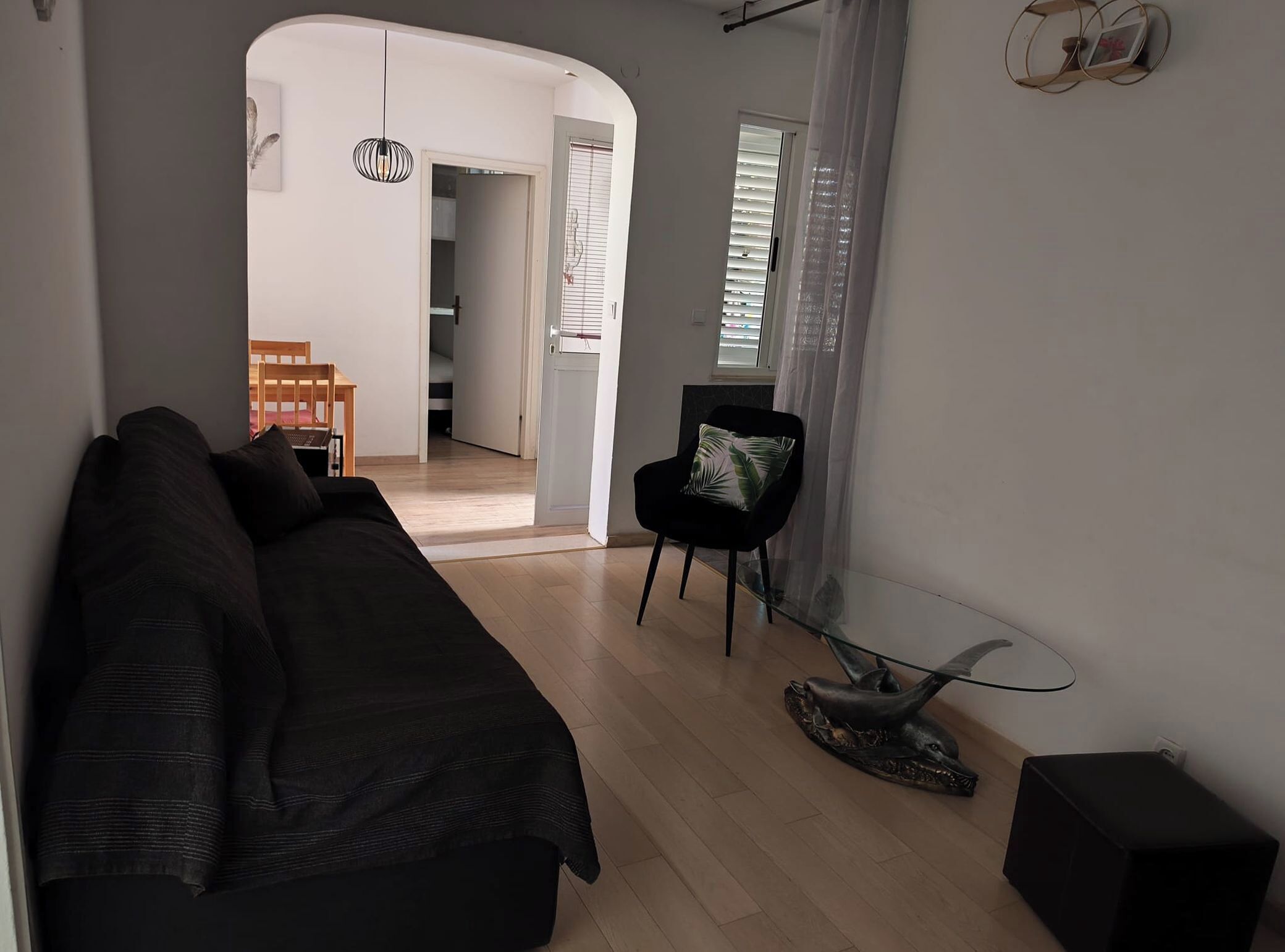 Un espace de vie moderne avec un canapé de couleur sombre, une table basse en verre et une chaise noire. On peut voir une petite sculpture sur la table et un haut-parleur sur le sol.