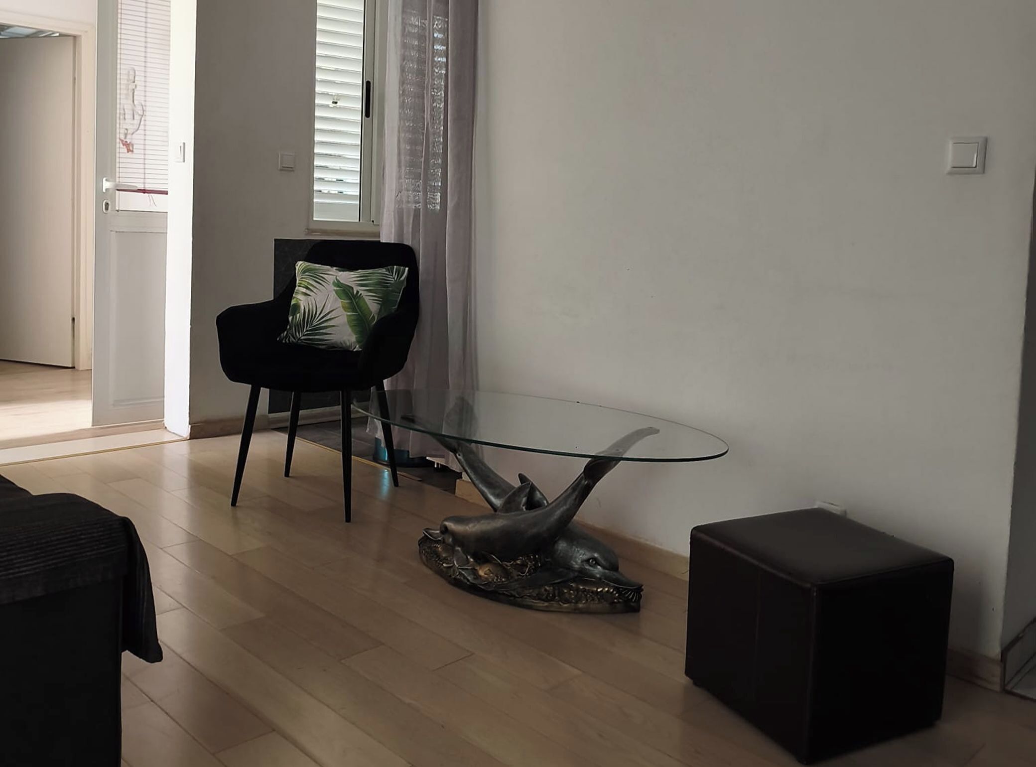 Ein modernes Wohnzimmer mit einem Glastisch, einem schwarzen Sessel mit gemustertem Kissen und einer dekorativen Skulptur auf dem Boden.