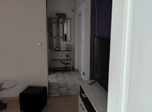 A narrow hallway with a television on the right, a small table with a chair on the left, and a door at the end. - Apartment Leonora (Dubrovnik)