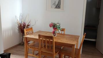 A dining area with a wooden table and chairs, a vase with flowers, and a framed artwork on the wall.
