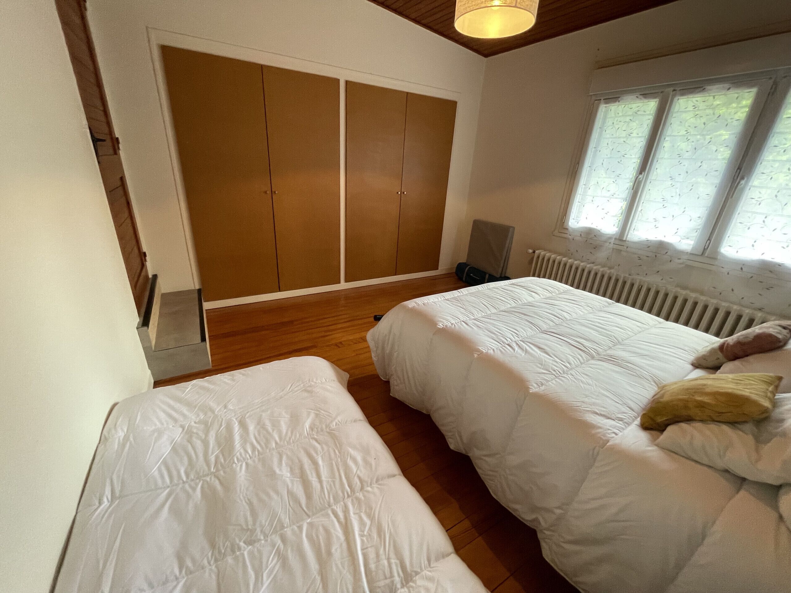 Ein Schlafzimmer mit zwei Betten, Holzboden, einem großen Kleiderschrank, einem Heizkörper und einem Fenster mit Blick.