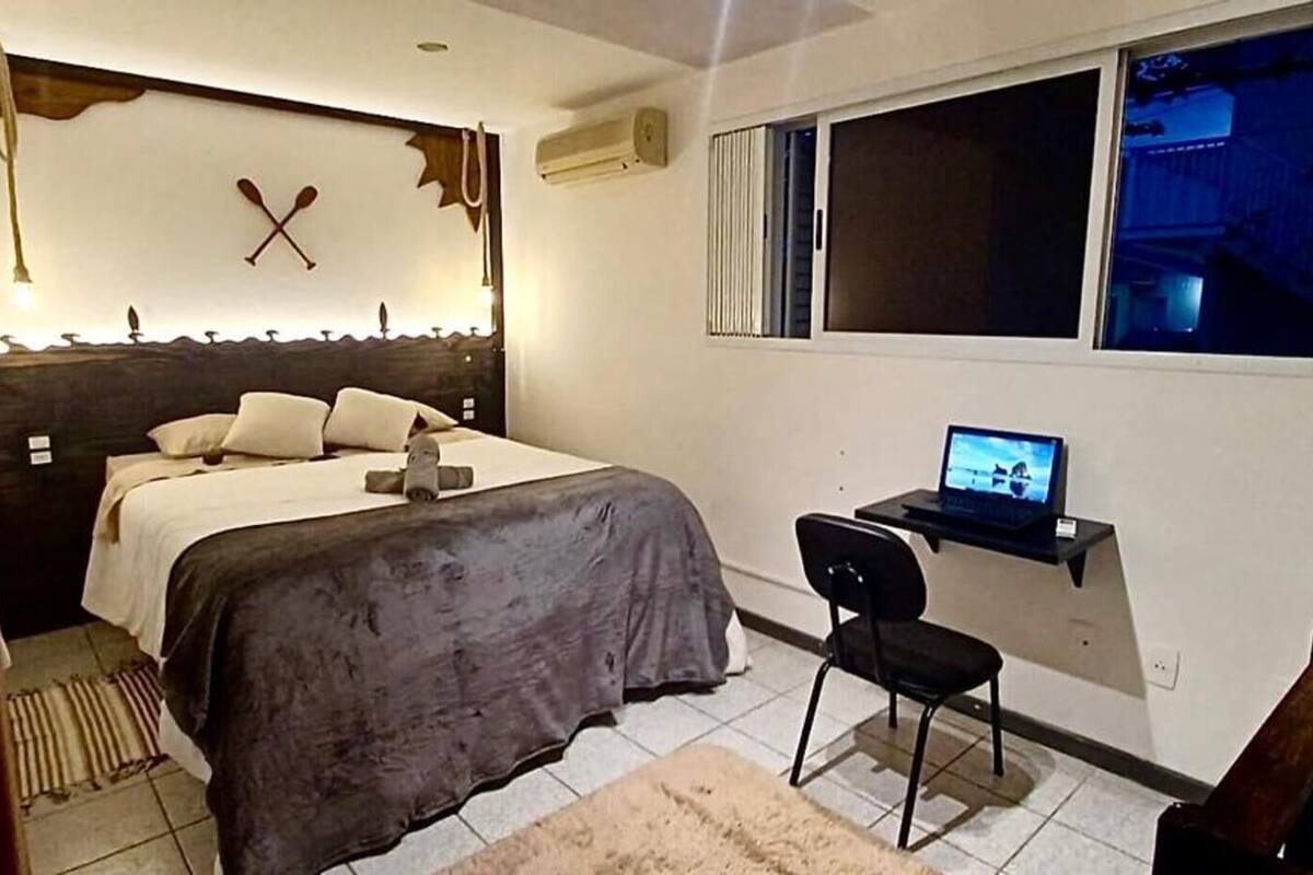 A bedroom with a bed, a desk with a laptop, a chair, and a window.