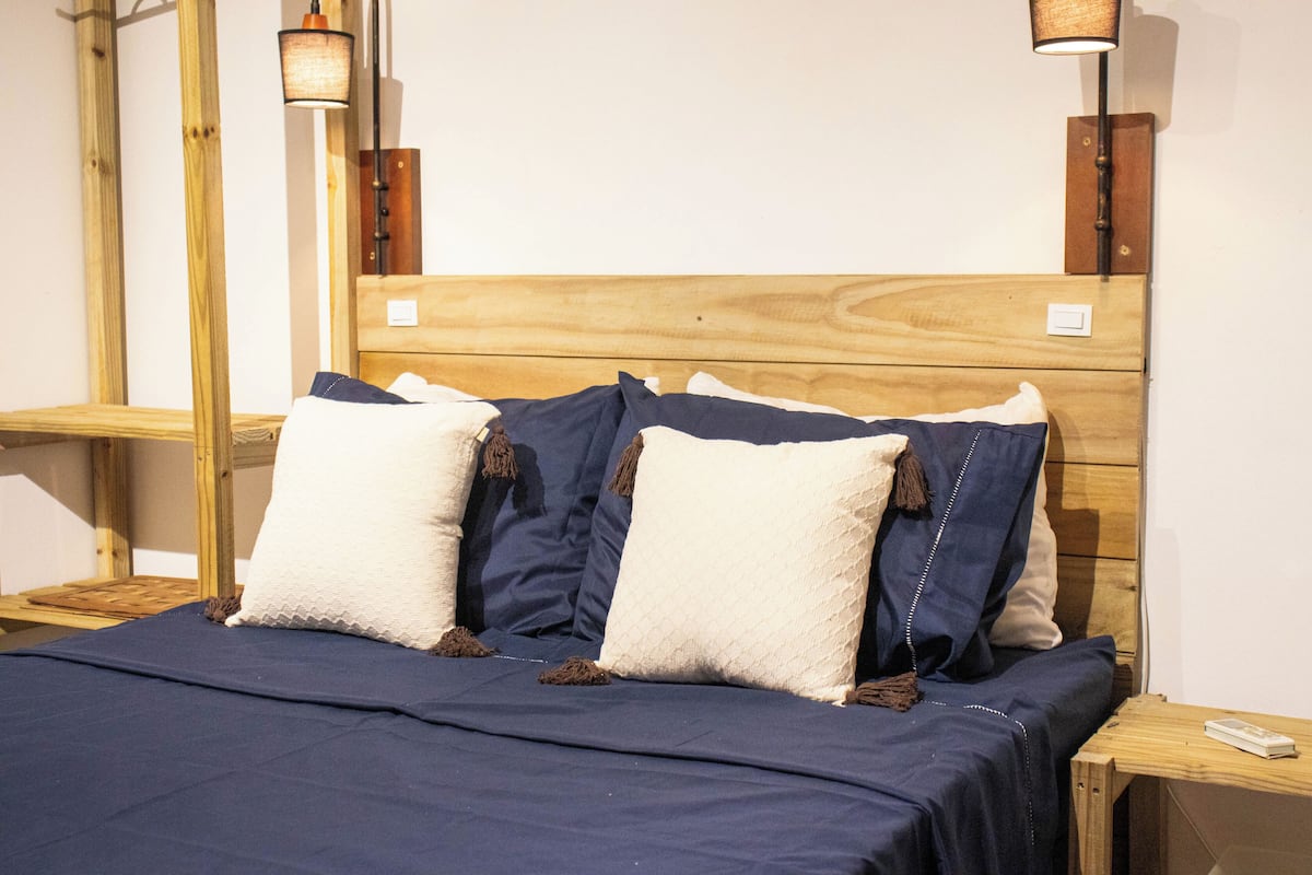 A neatly made bed with a dark blue bedspread, a wooden headboard, and two bedside tables with lamps.