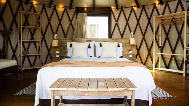A tented room with a large bed, wooden furniture, and a view of the outdoors. - Island Vibe Nomads - Adventure Hostels (Florianópolis)