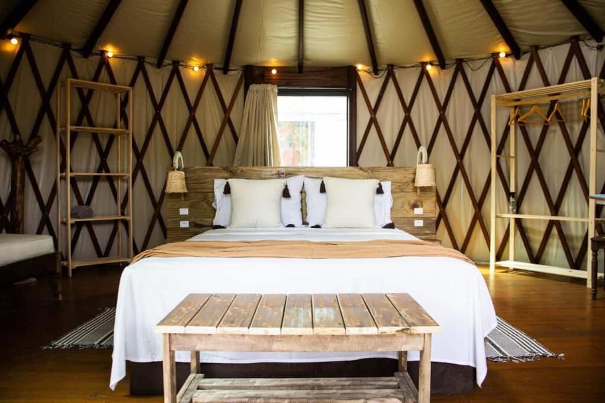 A tented room with a large bed, wooden furniture, and a view of the outdoors.