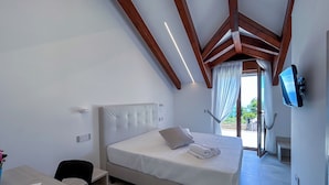 A bedroom with a bed, a desk, a chair, a TV, and a balcony with curtains. - CASA MILLY (Agerola)