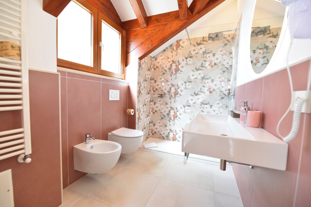 Un baño con bidé, inodoro y lavamanos, con vigas de madera y papel tapiz floral.