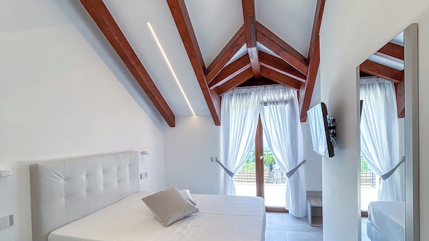 A bedroom with a large bed, wooden beams, and a view of the outdoors. - CASA MILLY (Agerola)