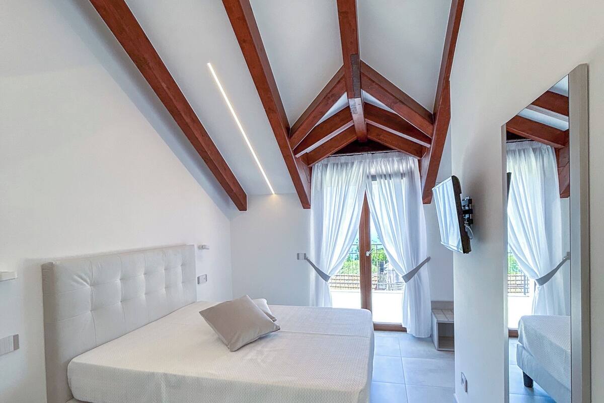 A bedroom with a large bed, wooden beams, and a view of the outdoors.