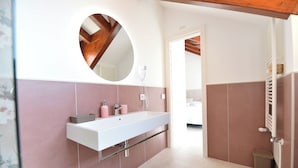 A modern bathroom with a white sink, pink tiles, a round mirror, and a shower area. - CASA MILLY (Agerola)