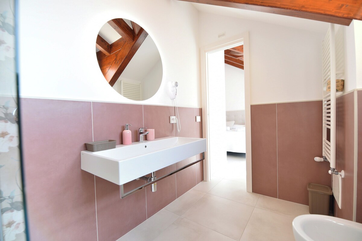 A modern bathroom with a white sink, pink tiles, a round mirror, and a shower area.