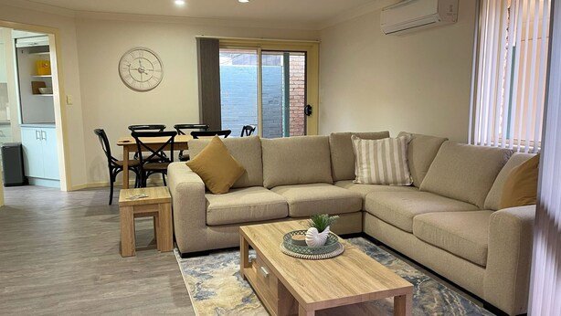 Una sala de estar con un sofá color beige, una mesa de centro de madera y un comedor con mesa y sillas.