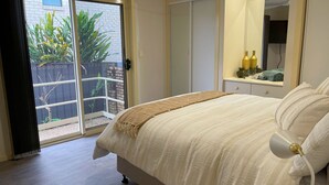Un dormitorio con cama, ventana y puerta corredera que da a un área exterior con plantas.