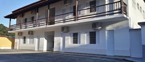 A two-story building with a balcony, air conditioning units, and a gated entrance.