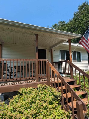A single-story mobile home with a wooden deck and a porch. - Charming 2-bedroom home in delightful downtown Indian River (indian river)