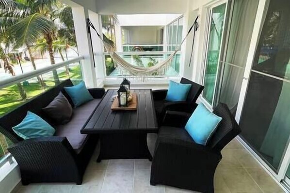 A covered outdoor seating area with a hammock, black cushioned chairs, and a central table with a lantern.