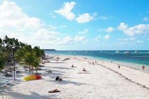 A beach with white sand, palm trees, and a clear blue sky.