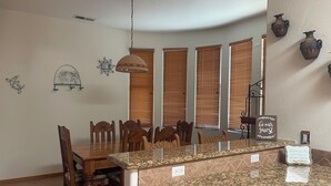 Een eethoek met houten stoelen en een granieten aanrecht, een hanglamp en decoratieve wanddecoratie.