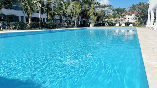 A clear blue pool surrounded by palm trees and a white building.