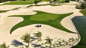 A golf course with sand bunkers, a water hazard, and palm trees.