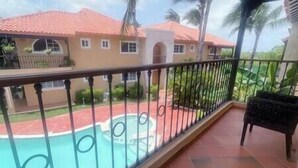 Un balcon donnant sur une piscine et un bâtiment dont le toit est recouvert de tuiles rouges.