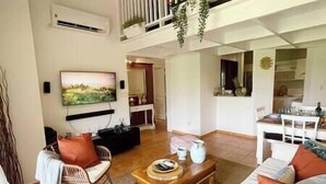 Un vaste espace de vie comprenant une table basse en bois, un canapé et un téléviseur fixé au mur.