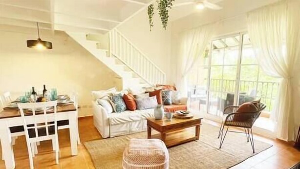 Un salon spacieux avec un canapé blanc, une table à manger et une table basse. Un escalier mène à un niveau supérieur.