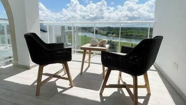 Varanda com duas cadeiras de vime preto e uma mesa pequena, com vista para um rio e vegetação.