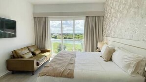 Quarto de hotel com uma cama grande, um sofá e vista para um corpo d'água através de amplas janelas.
