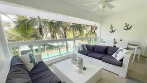 A modern living room with a white sofa, a coffee table, and a view of a pool and palm trees.