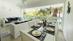 A dining area with a table set for four, a sofa, and a view of palm trees through a large window.