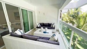 A balcony with a white sofa, a small table with decorative items, and a view of palm trees.