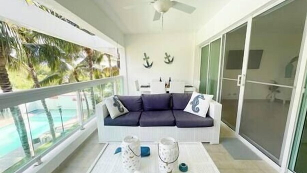 A balcony with a white sofa, two decorative vases, and a view of a pool and palm trees.