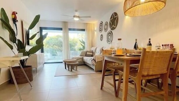 Un salon moderne avec un canapé, une table à manger et des chaises. Une grande fenêtre laisse entrer la lumière naturelle et offre une vue sur la verdure environnante.