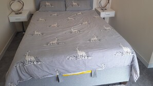 En säng med ett grått sängöverkast med kaninmotiv, två sängbord med ringar på och en grå sänggavel.