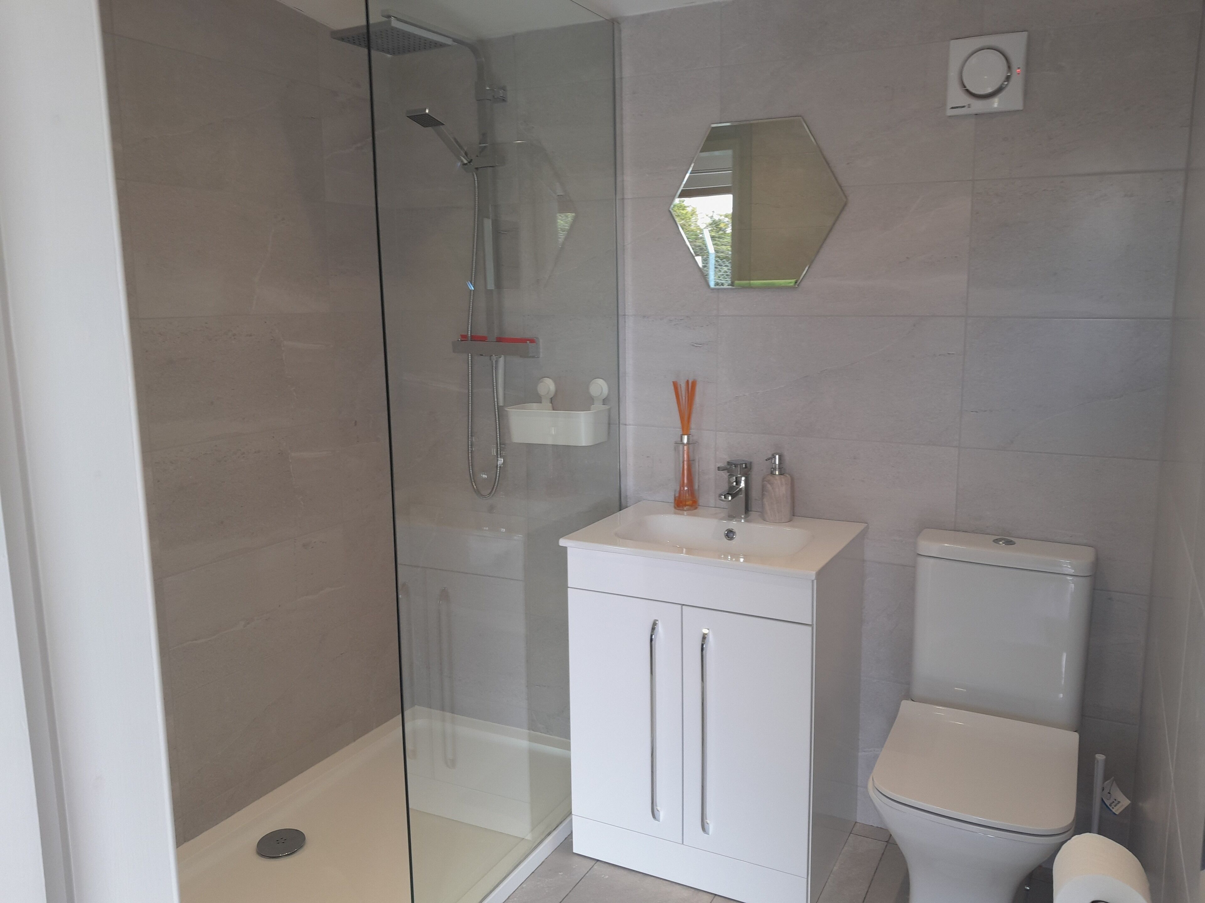 A modern bathroom with a glass-enclosed shower, a white sink with a mirror above it, and a toilet.