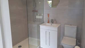 Ett modernt badrum med en dusch som är avskärmad med glasväggar, en vit tvättställ med en spegel ovanför och en toalett.