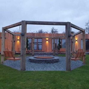 A wooden gazebo with a circular stone floor, surrounded by chairs, set in a grassy area. - Furness View Barn Retreat (Dalton-in-Furness)