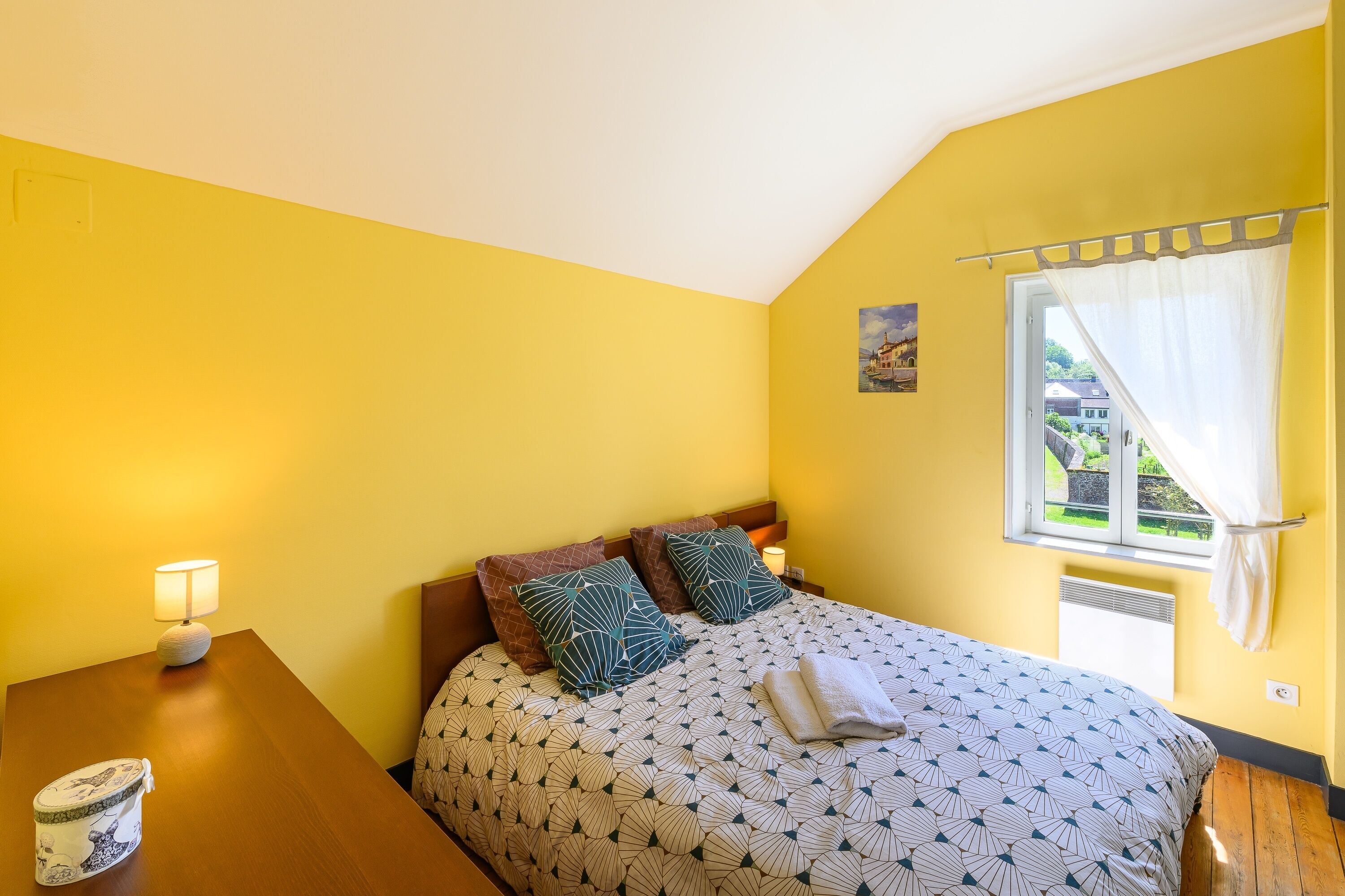 Un dormitorio con cama, mesita de noche, lámpara y ventana con cortinas.