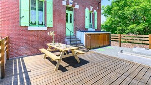 A wooden deck with a picnic table and benches, a brick building with green shutters, and a wooden fence.