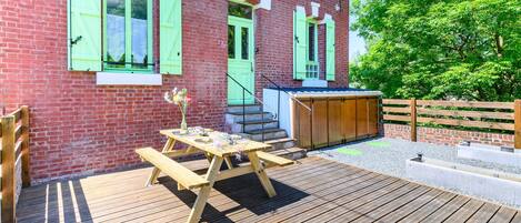 A wooden deck with a picnic table and benches, a brick building with green shutters, and a wooden fence.
