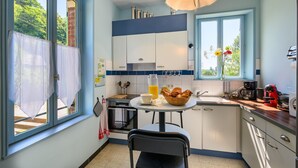 A kitchen with a dining table, a coffee maker, and a window with flowers.