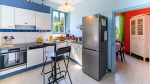 A modern kitchen with white cabinets, a stainless steel refrigerator, and a dining area with a table and chairs.